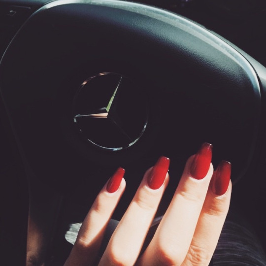 Девушка с красным лаком на ногтях за рулём Мерседе