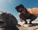 Парень в очках на пляже и большая черепаха
