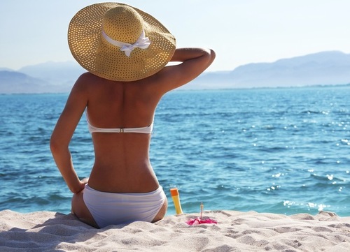 Девушка в белом купальнике и шляпе смотрит на море