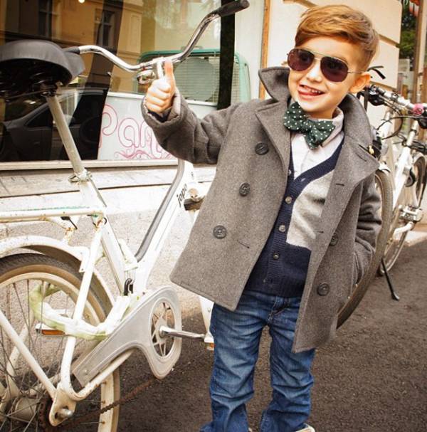 Мальчик в пальто, джинсах и очках у велосипеда