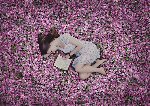 Девушка на розовой цветочной поляне читает книгу